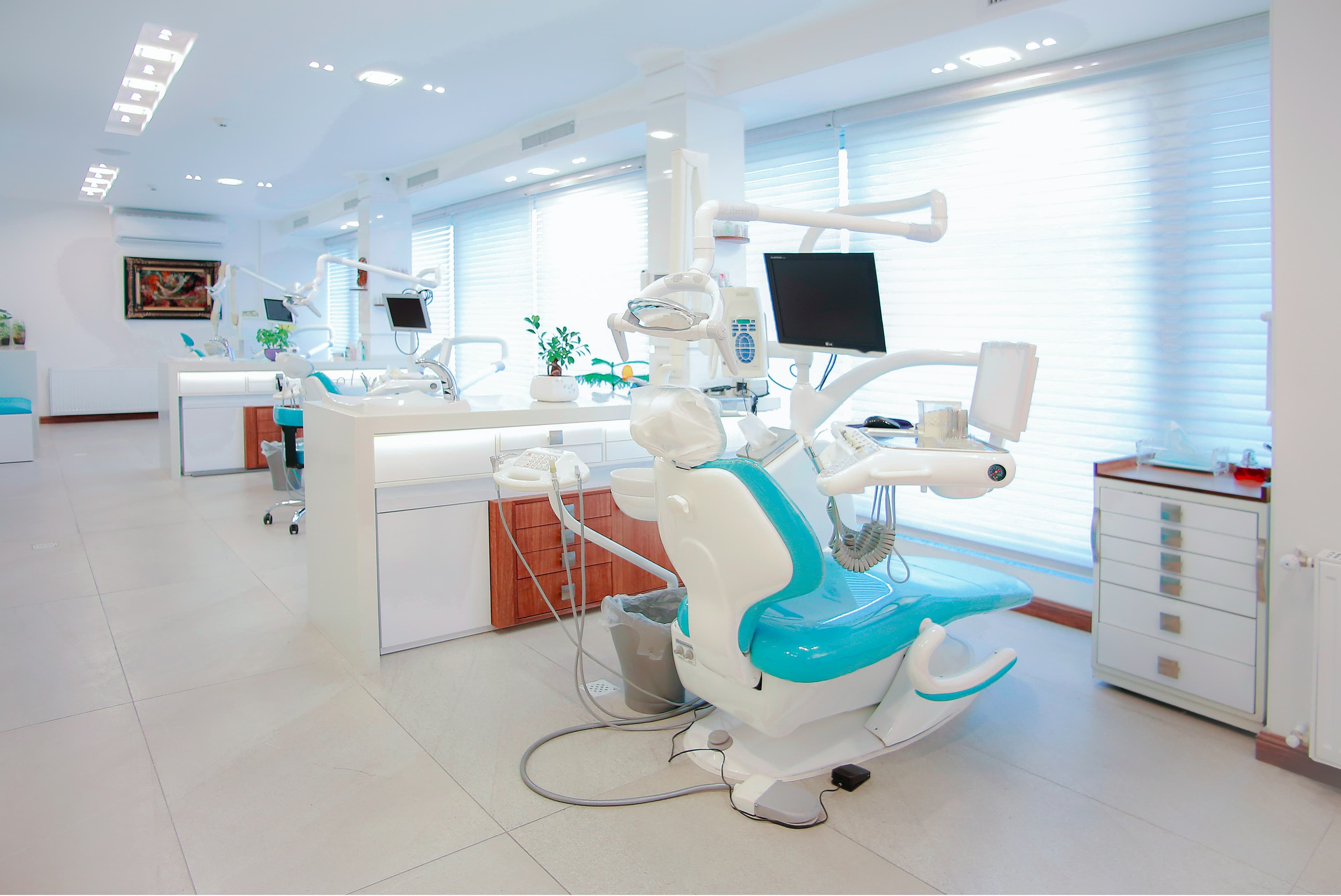 Modern dental operatory with teal treatment chair in a bright open-plan dental practice